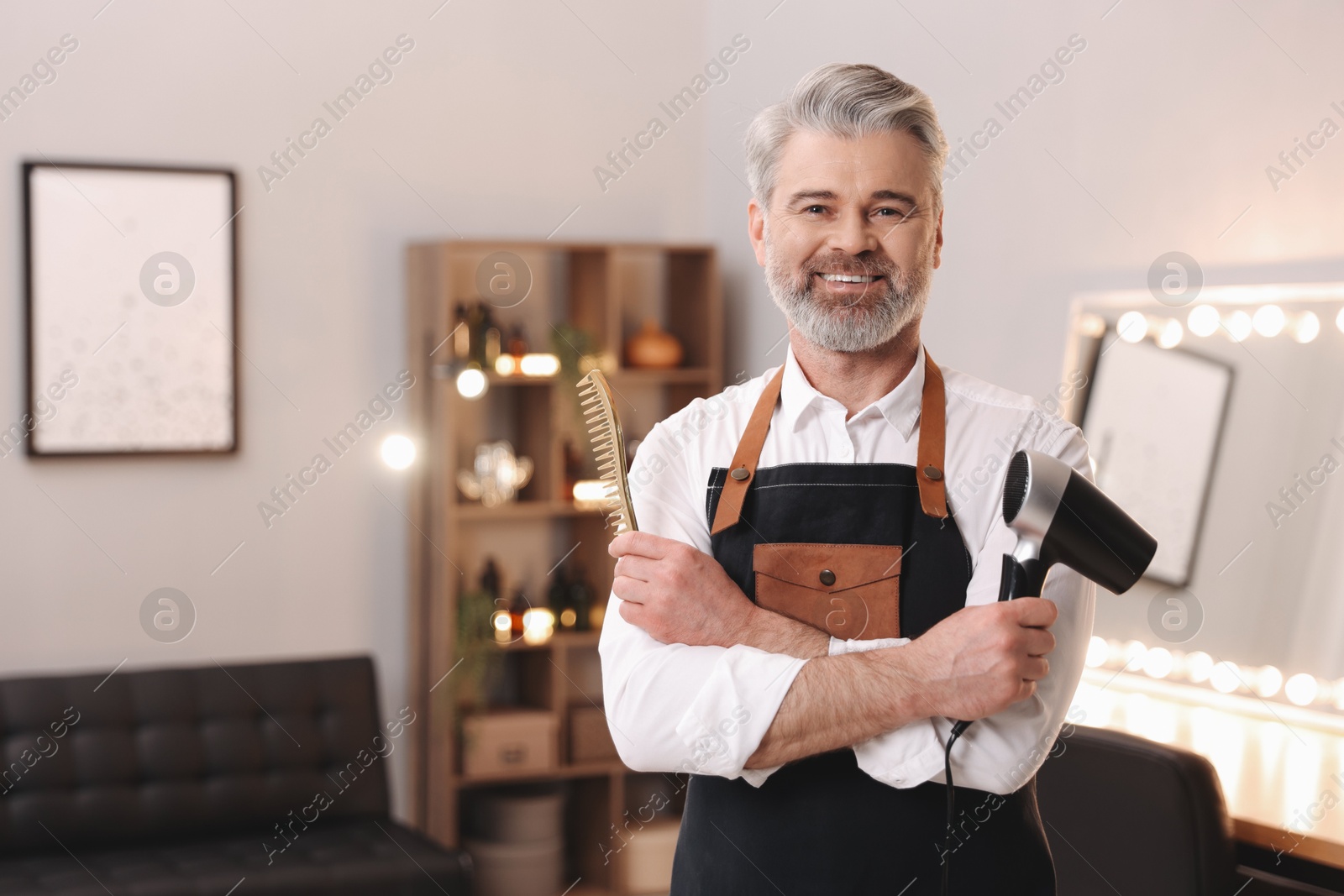 Photo of Smiling hairdresser with dryer and comb in beauty salon, space for text