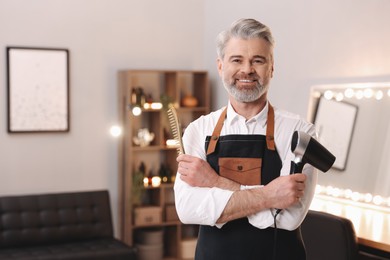 Smiling hairdresser with dryer and comb in beauty salon, space for text