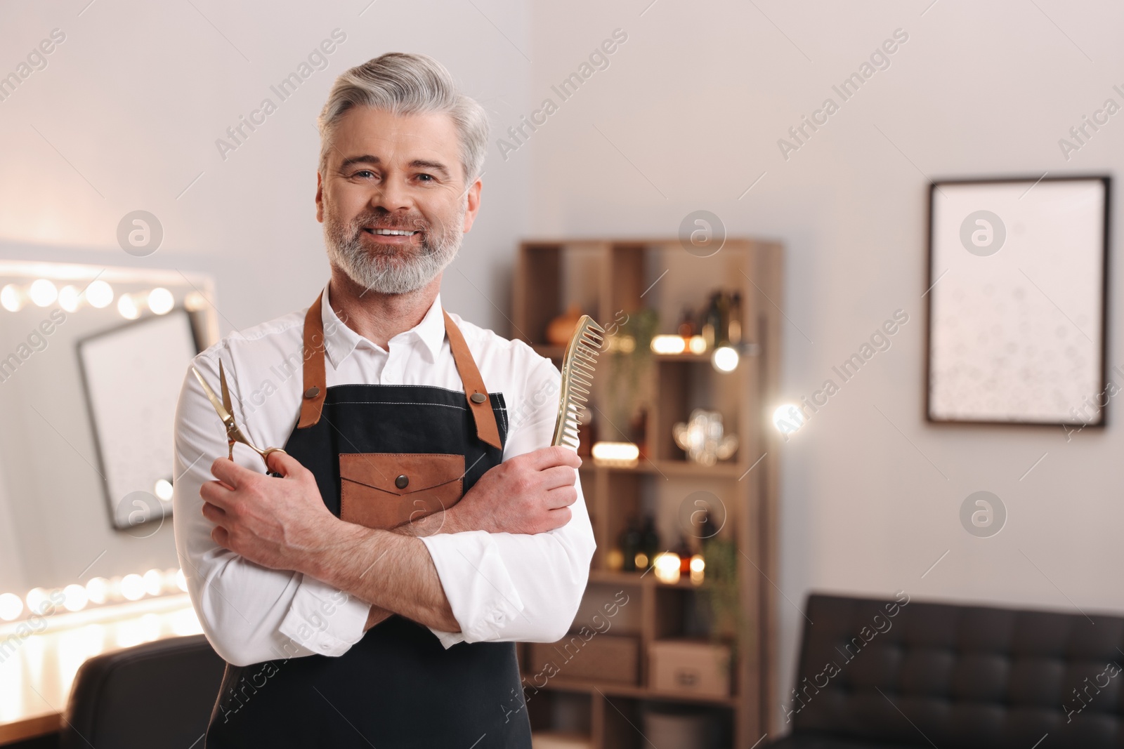 Photo of Smiling hairdresser with scissors and comb in beauty salon, space for text