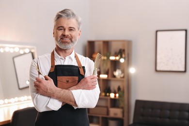 Smiling hairdresser with scissors and comb in beauty salon, space for text