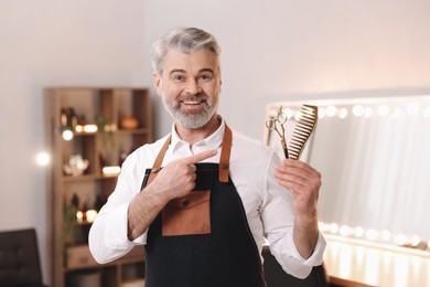 Smiling hairdresser with scissors and comb in beauty salon