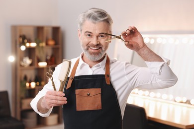 Photo of Smiling hairdresser with scissors and comb in beauty salon