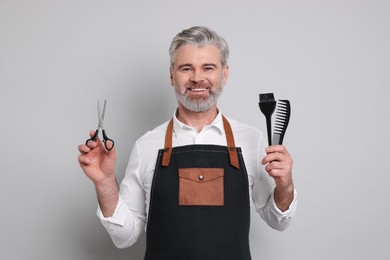 Smiling hairdresser with scissors, comb and hair dye brush on gray background