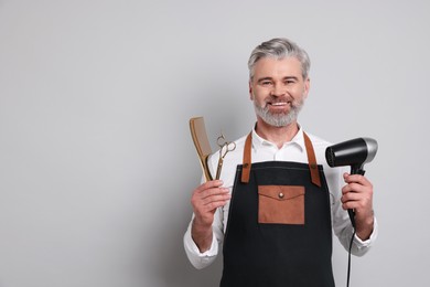 Smiling hairdresser with dryer, scissors and comb on gray background, space for text