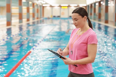 Swimming coach taking notes at indoor pool. Space for text