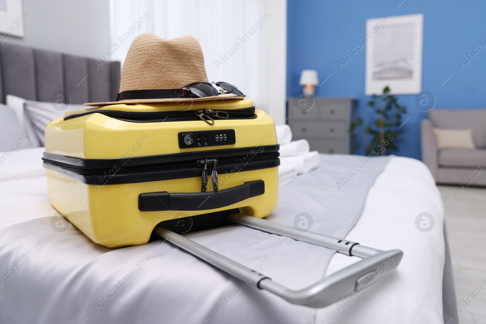 Suitcase with hat and sunglasses on bed in hotel room Photo of Suitcase with hat and sunglasses on bed in hotel room