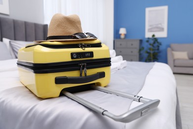 Photo of Suitcase with hat and sunglasses on bed in hotel room