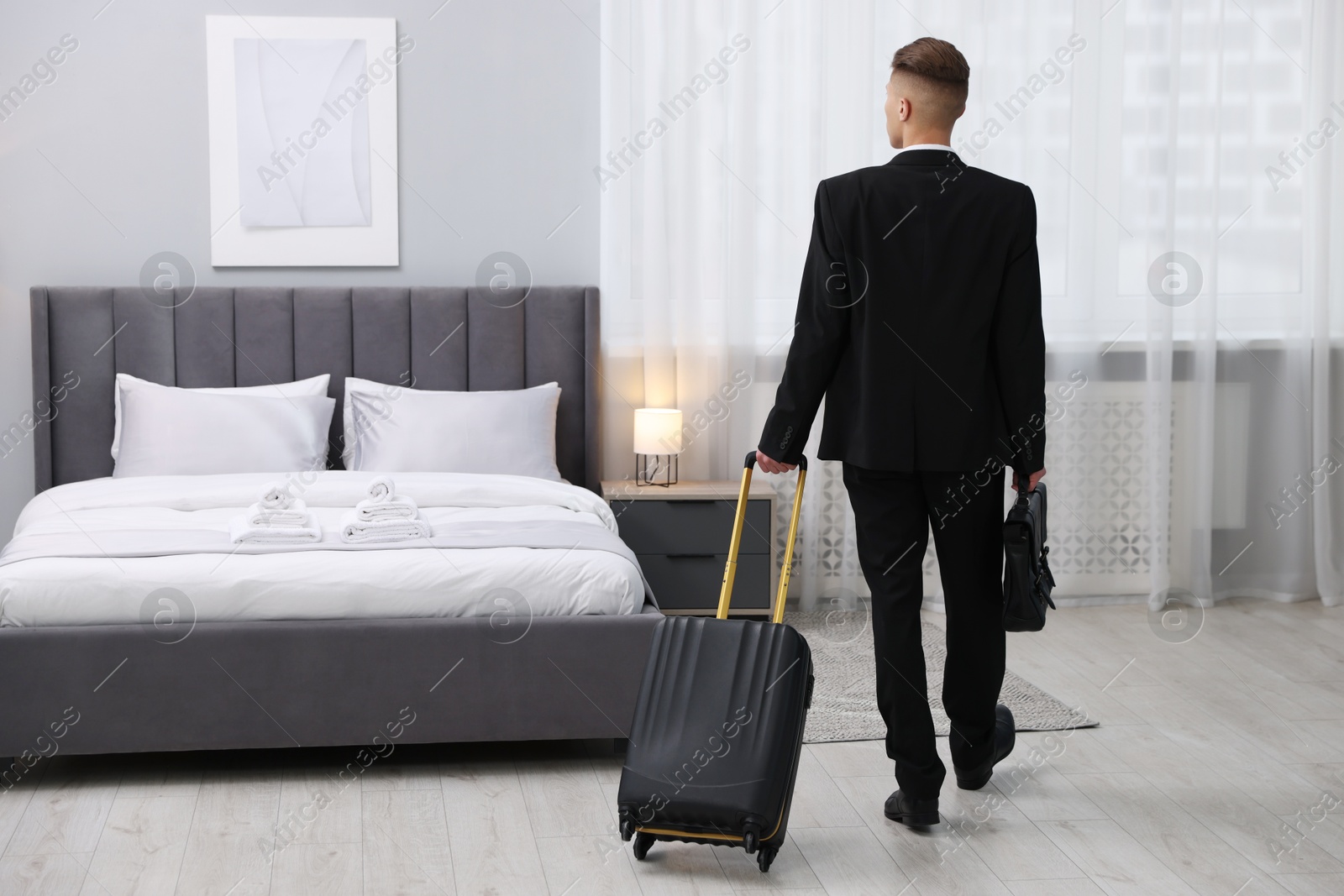 Photo of Businessman with suitcase in hotel room, back view