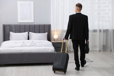 Businessman with suitcase in hotel room, back view