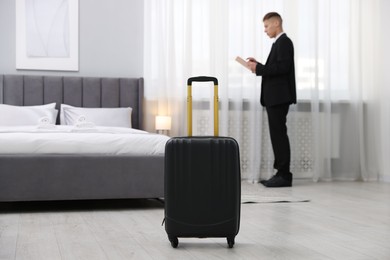 Stylish suitcase and businessman in hotel room, selective focus