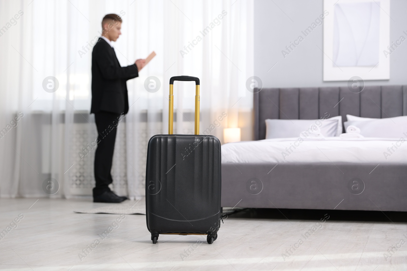 Photo of Stylish suitcase and businessman in hotel room, selective focus