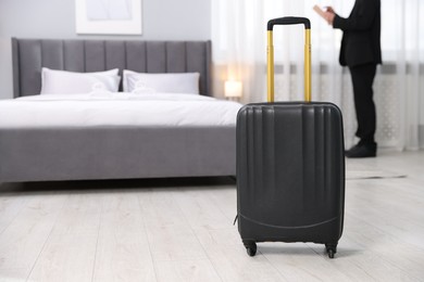 Stylish suitcase and businessman in hotel room, selective focus