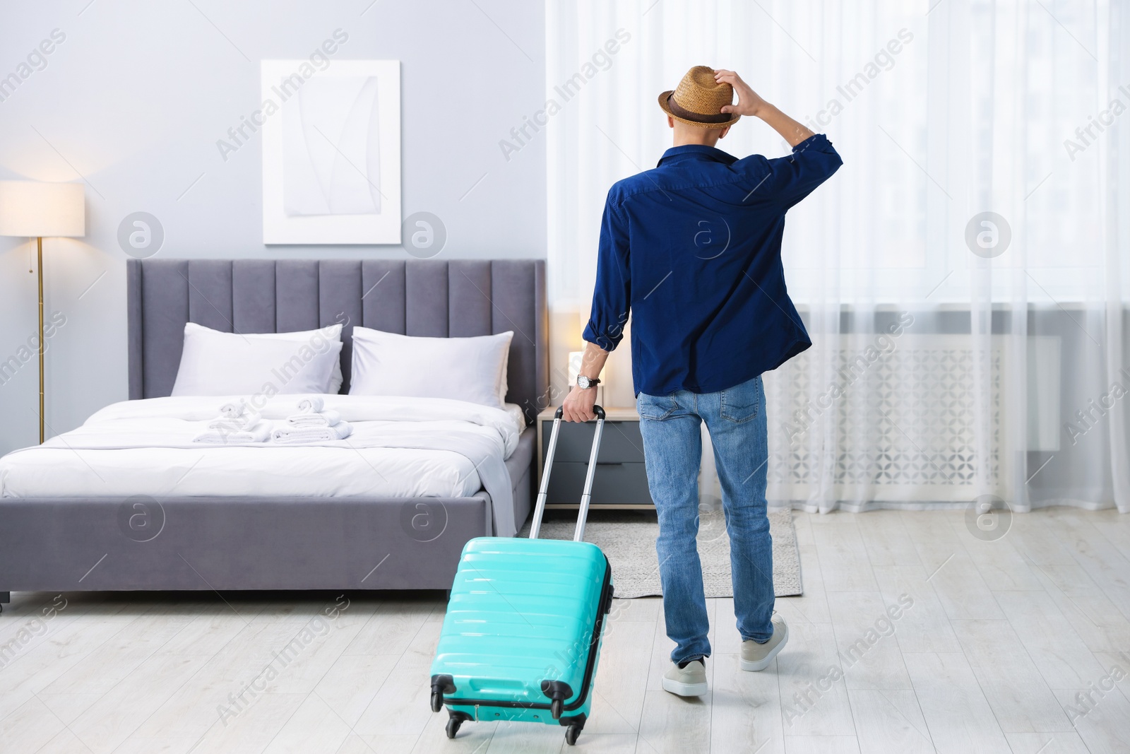 Photo of Man with suitcase in hotel room, back view