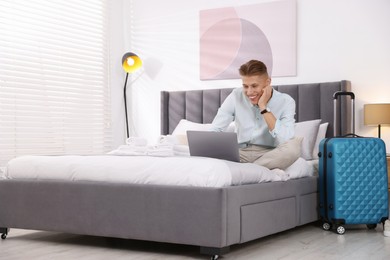 Man with laptop on bed in his hotel room. Space for text