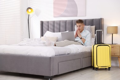 Photo of Man with laptop on bed in his hotel room