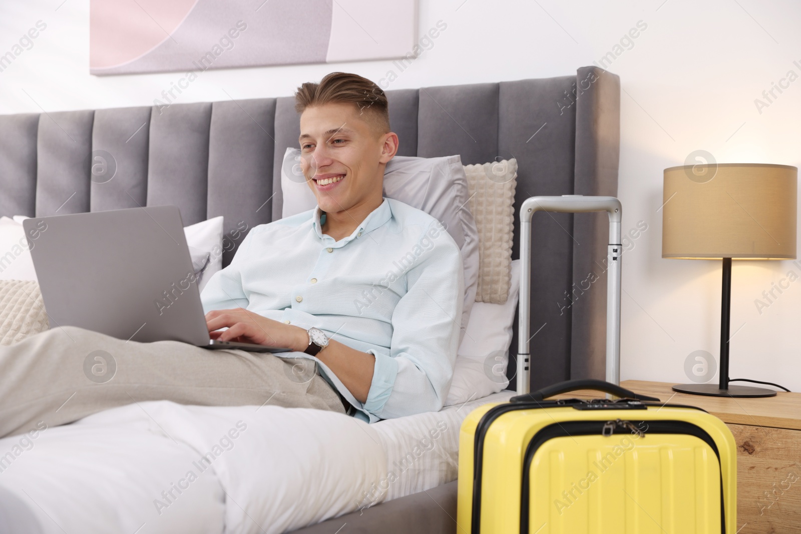 Photo of Man with laptop on bed in his hotel room