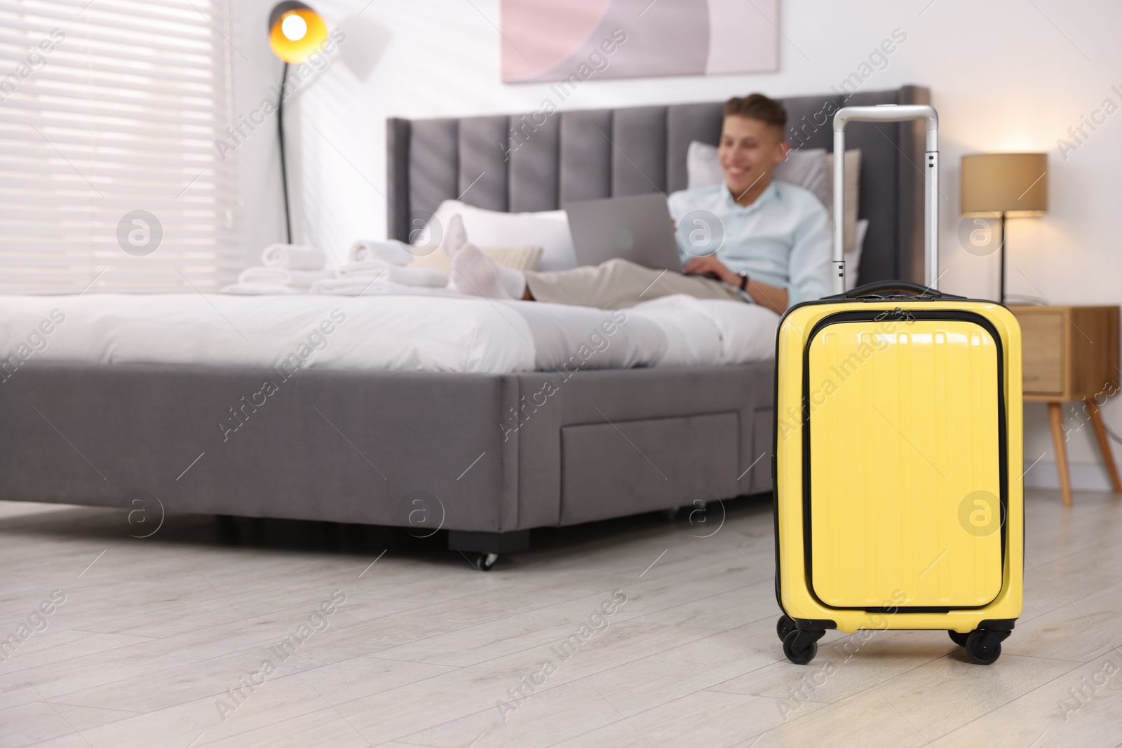 Photo of Suitcase and man with laptop on bed in his hotel room, selective focus