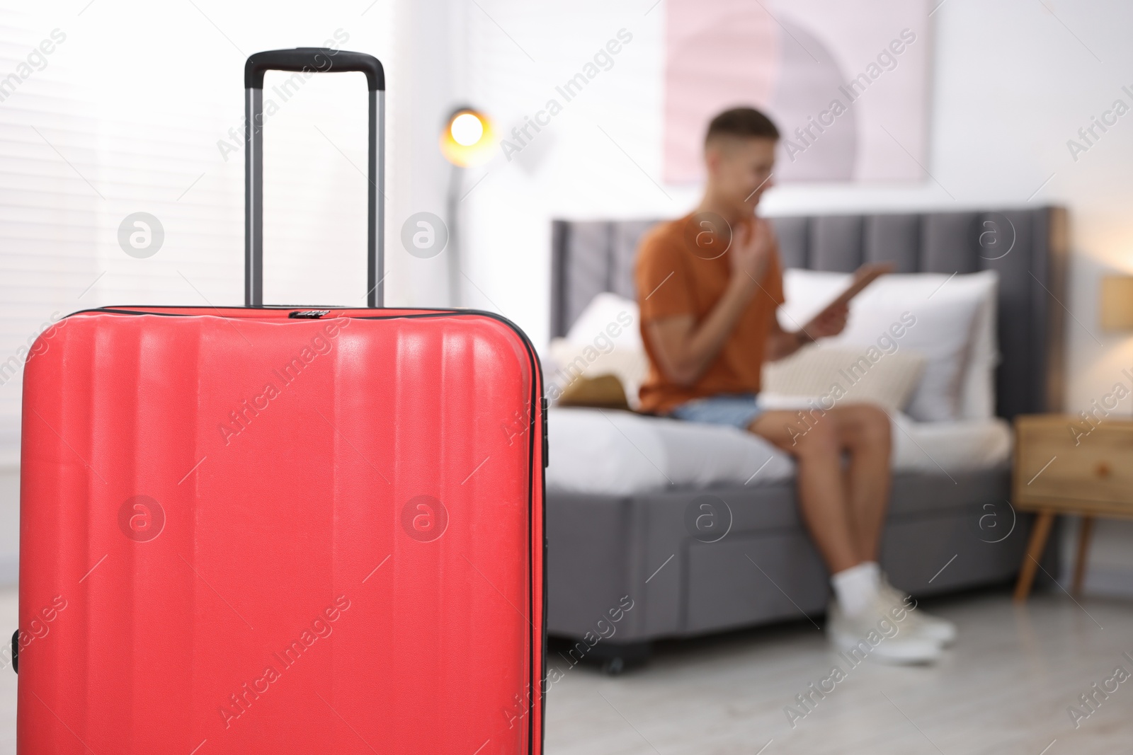 Photo of Suitcase and man with tablet on bed in his hotel room, selective focus