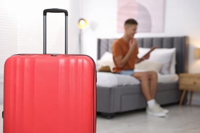 Suitcase and man with tablet on bed in his hotel room, selective focus