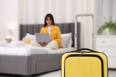 Suitcase and woman with laptop on bed in her hotel room, selective focus