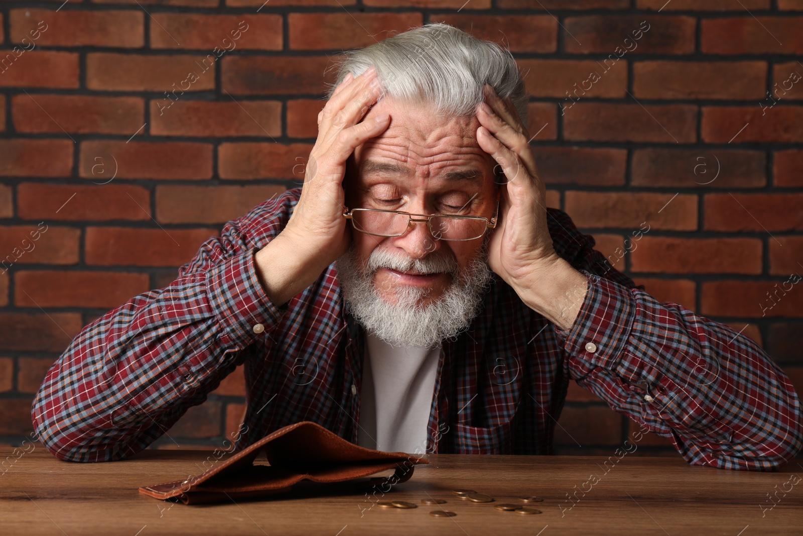 Photo of Upset senior man at wooden table with empty wallet and coins