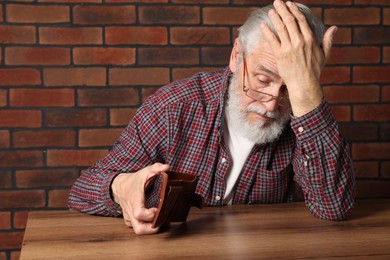 Upset senior man with empty wallet at wooden table. Financial problems