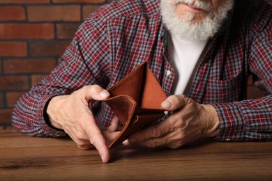 Senior man with empty wallet at wooden table, closeup. Financial problems