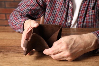 Photo of Senior man with empty wallet at wooden table, closeup. Financial problems