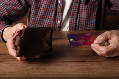 Photo of Senior man with empty wallet and credit card at wooden table, closeup. Financial problems