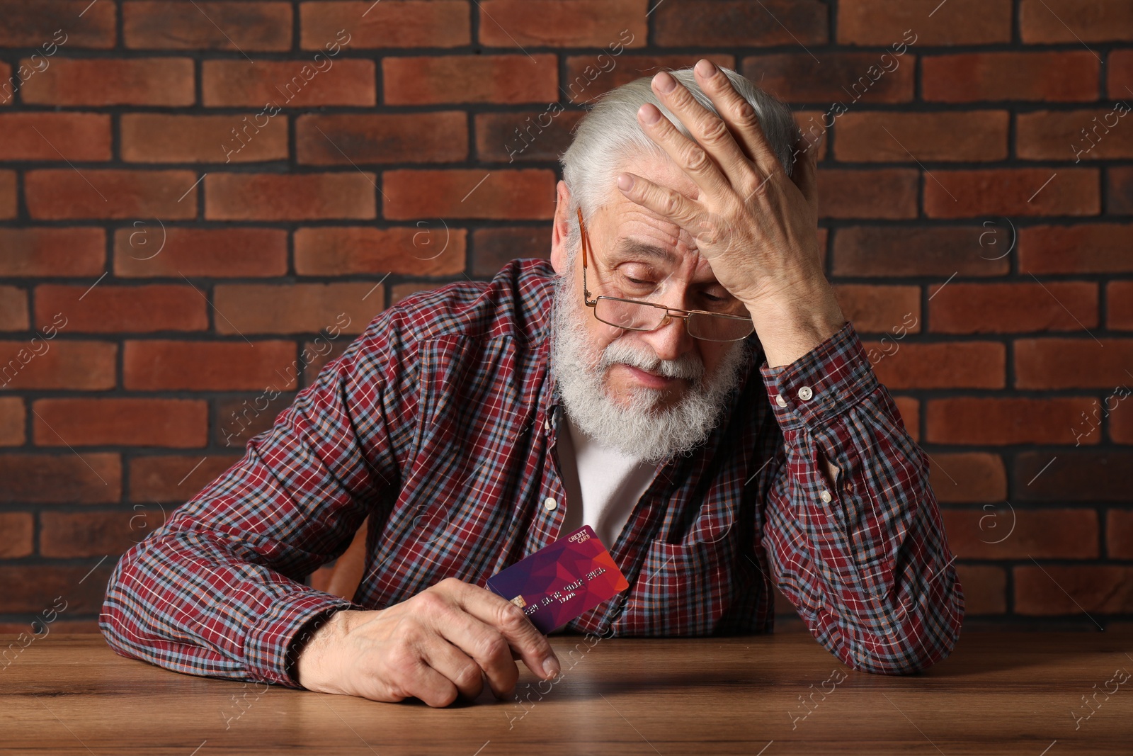 Photo of Upset senior man with credit card at wooden table. Financial problems