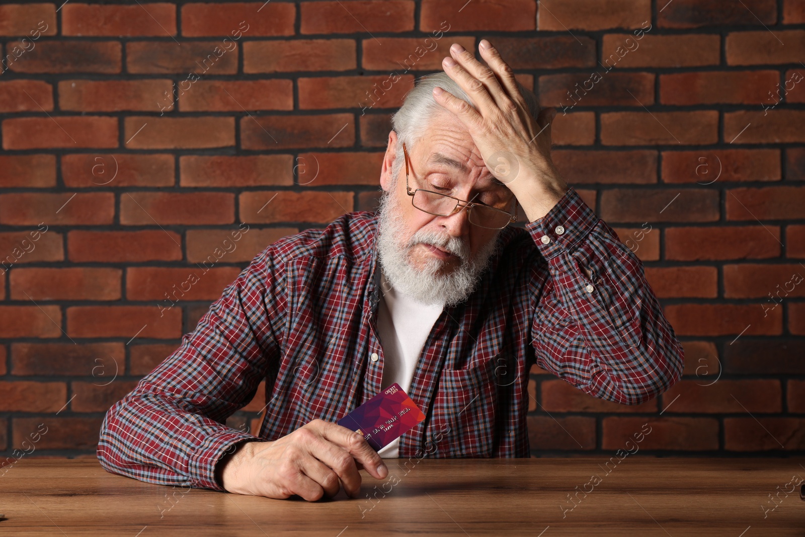 Photo of Upset senior man with credit card at wooden table. Financial problems