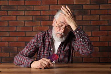 Upset senior man with credit card at wooden table. Financial problems