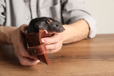 Photo of Senior man holding wallet with rat at wooden table, closeup. Financial problems