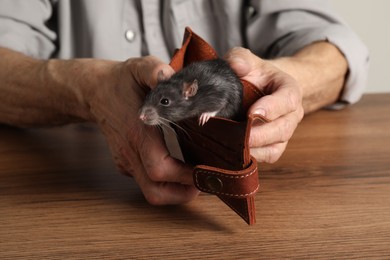 Senior man holding wallet with rat at wooden table, closeup. Financial problems