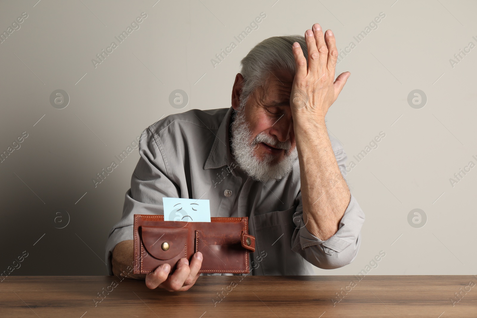 Photo of Upset senior man holding wallet with drawn sad face at wooden table. Financial problems