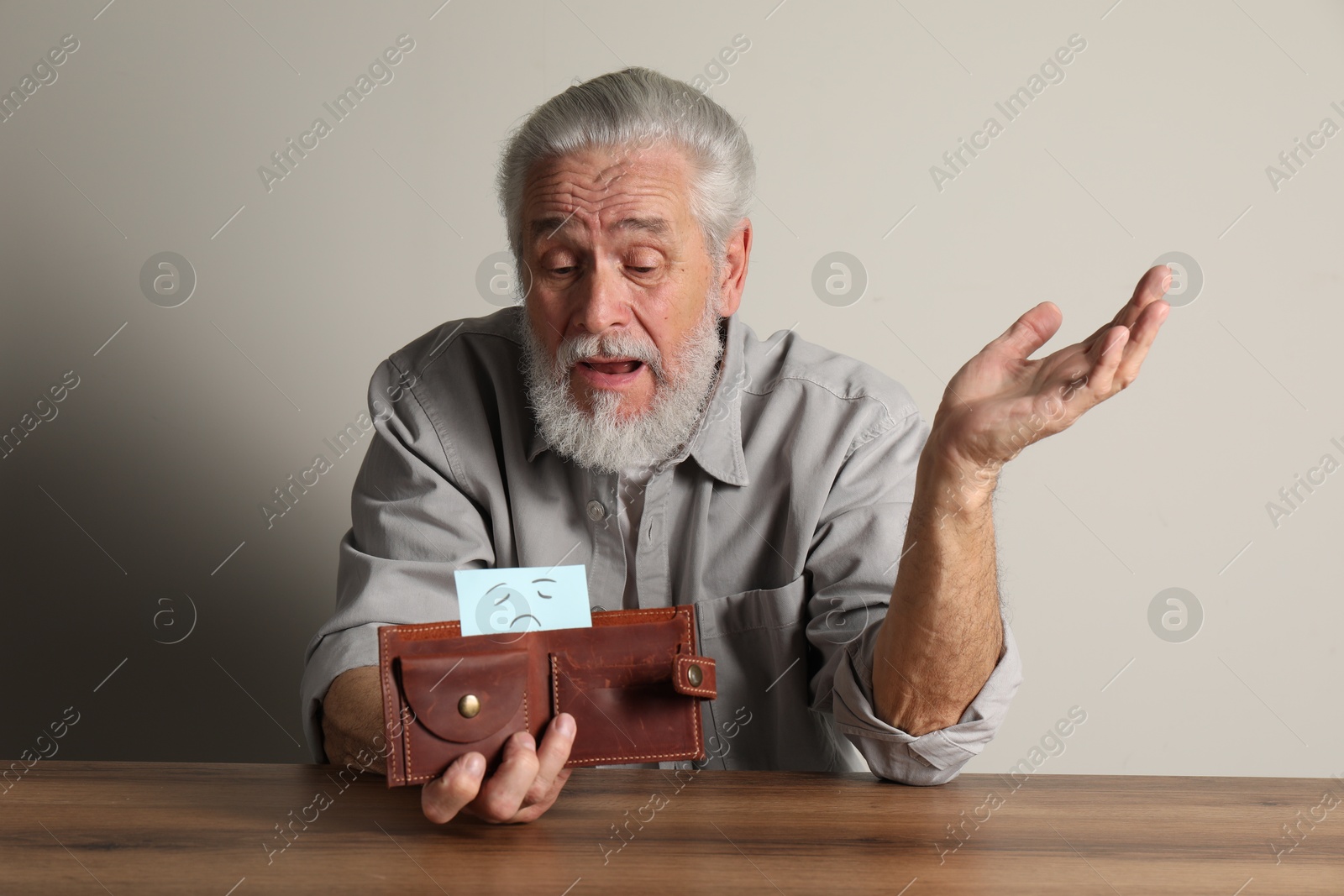 Photo of Upset senior man holding wallet with drawn sad face at wooden table. Financial problems