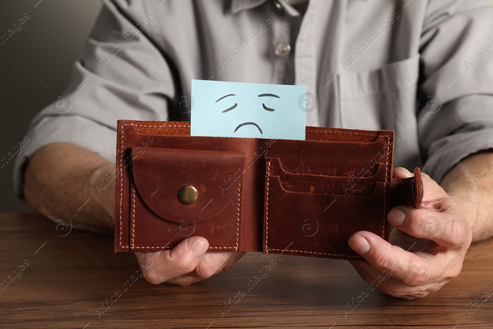 Photo of Senior man holding wallet with drawn sad face at wooden table, closeup. Financial problems