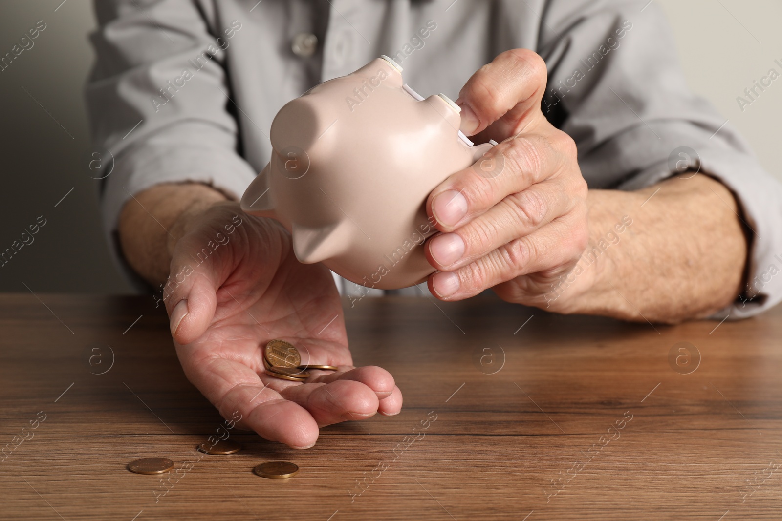 Photo of Senior man trying to get something out from piggy bank at wooden table, closeup. Financial problems