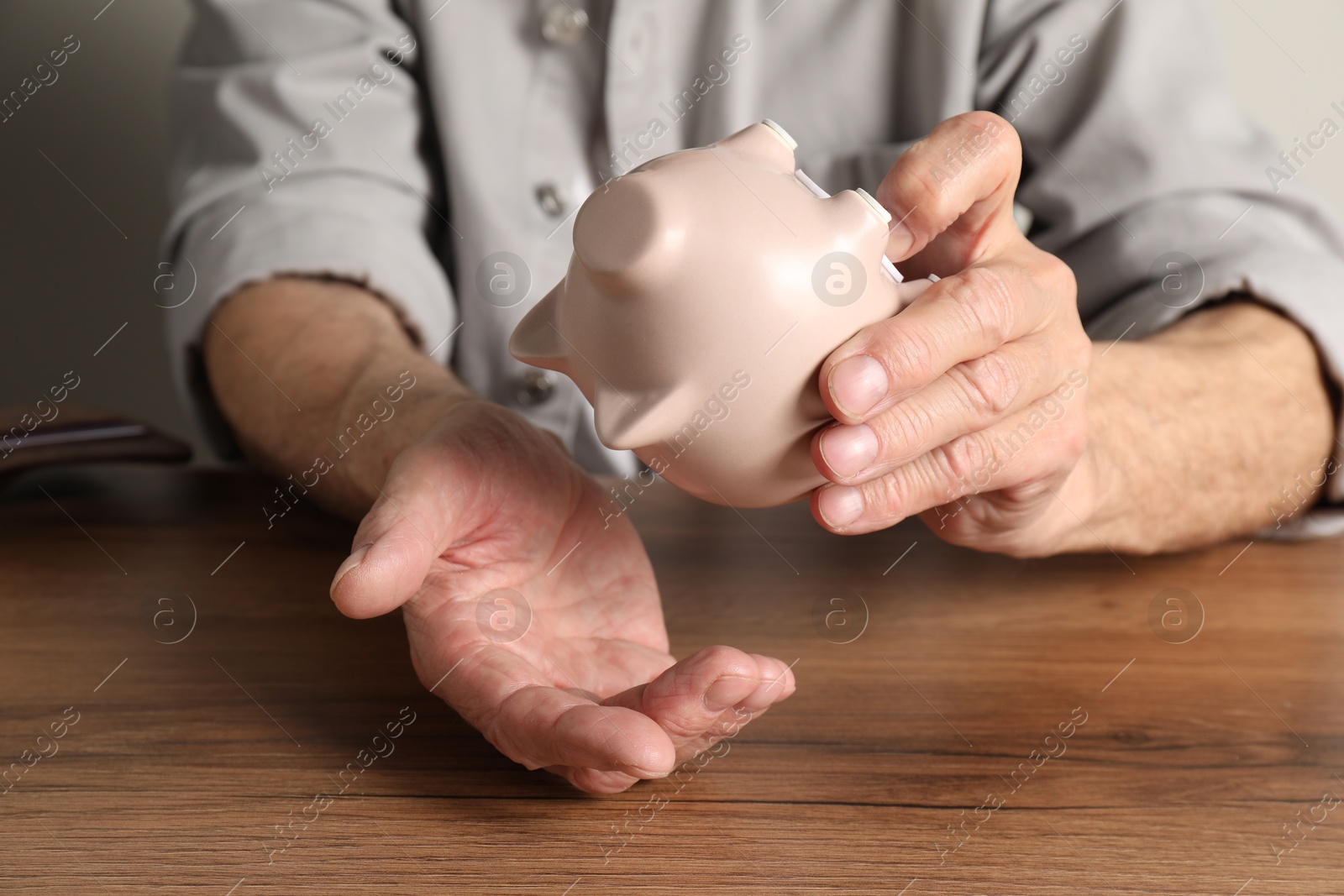 Photo of Senior man trying to get something out from piggy bank at wooden table, closeup. Financial problems