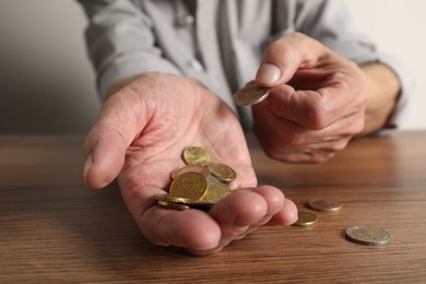 Photo of Senior man counting coins at wooden table, closeup. Financial problems