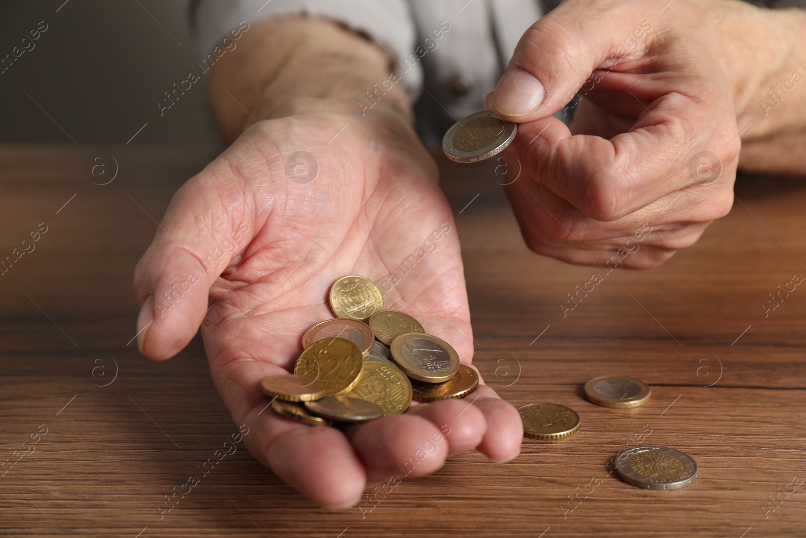 Photo of Senior man counting coins at wooden table, closeup. Financial problems