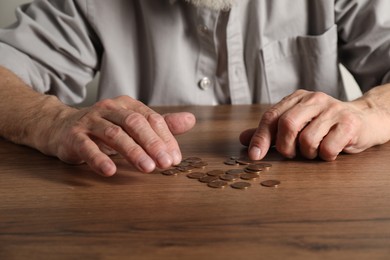 Senior man counting coins at wooden table, closeup. Financial problems