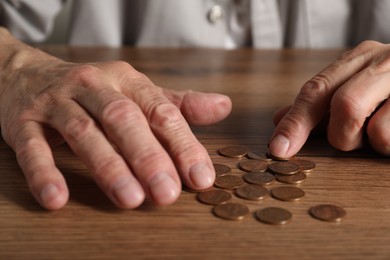 Photo of Senior man counting coins at wooden table, closeup. Financial problems