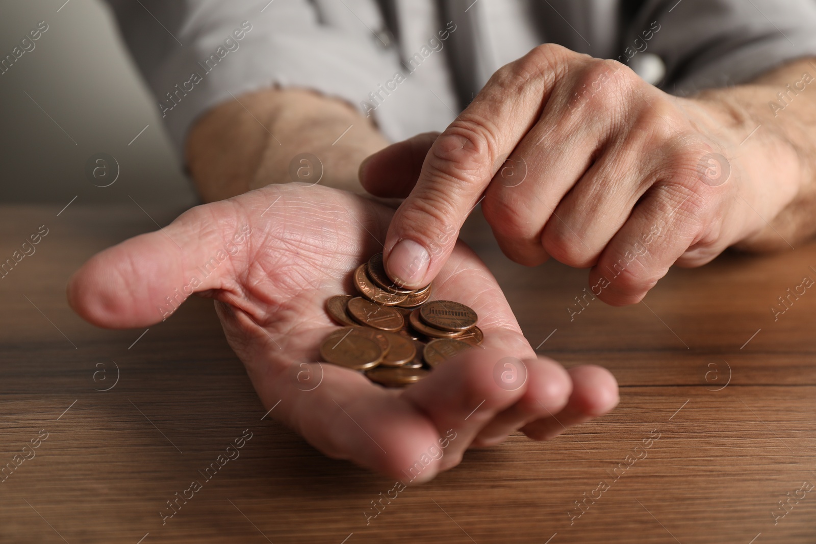 Photo of Senior man counting coins at wooden table, closeup. Financial problems