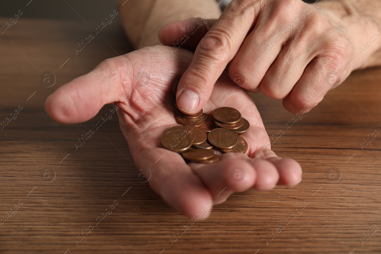 Photo of Senior man counting coins at wooden table, closeup. Financial problems