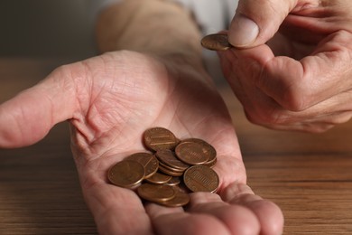 Photo of Senior man counting coins at wooden table, closeup. Financial problems