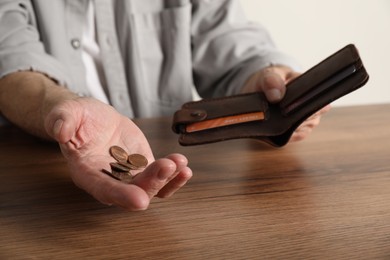 Photo of Senior man with coins and wallet at wooden table, closeup. Financial problems