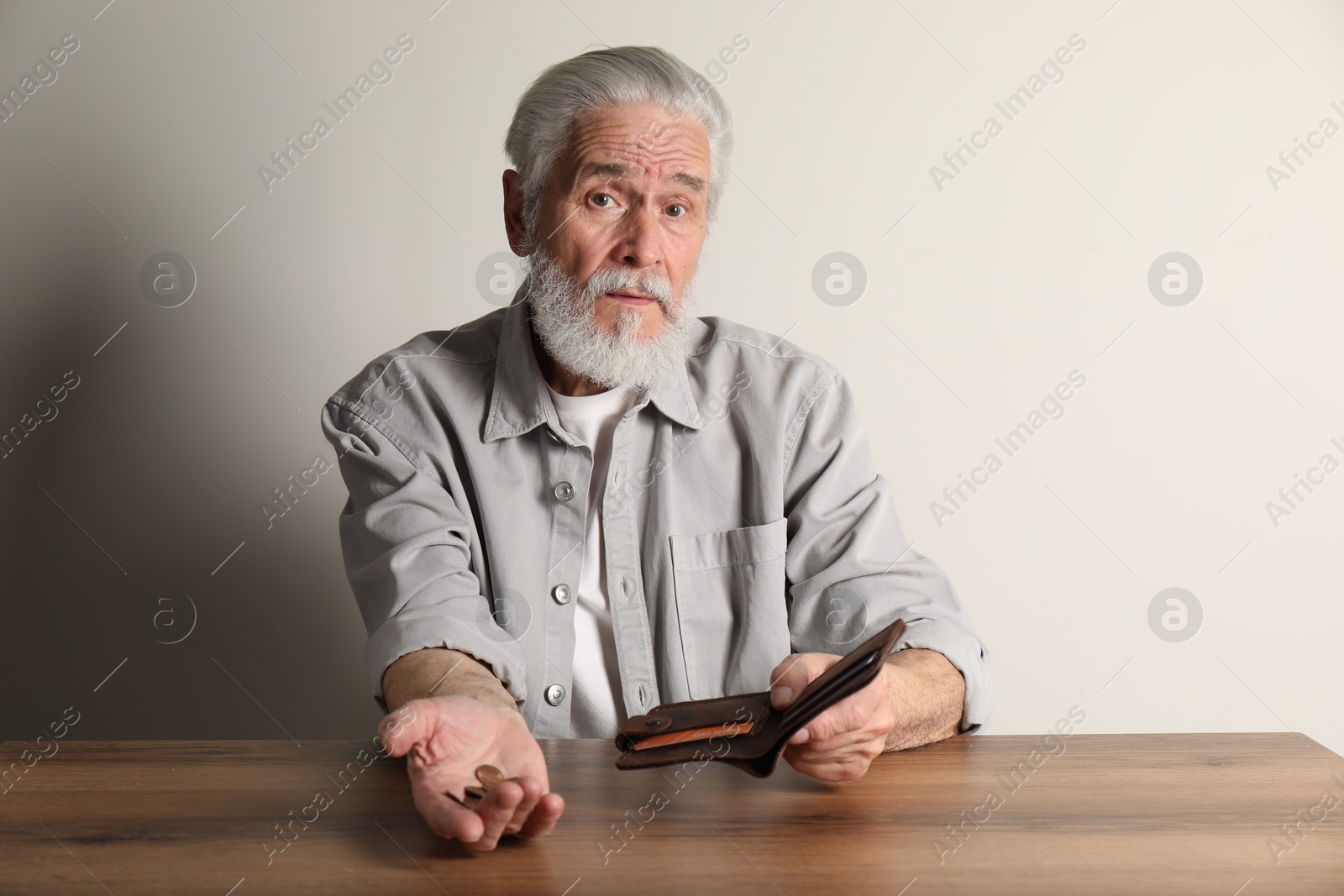 Photo of Upset senior man with coins and wallet at wooden table. Financial problems