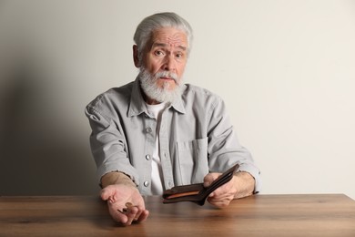 Upset senior man with coins and wallet at wooden table. Financial problems