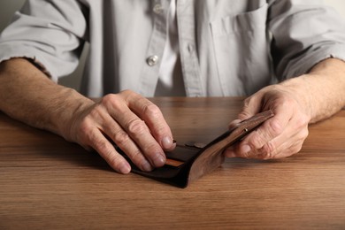 Photo of Senior man with wallet counting coins at wooden table, closeup. Financial problems